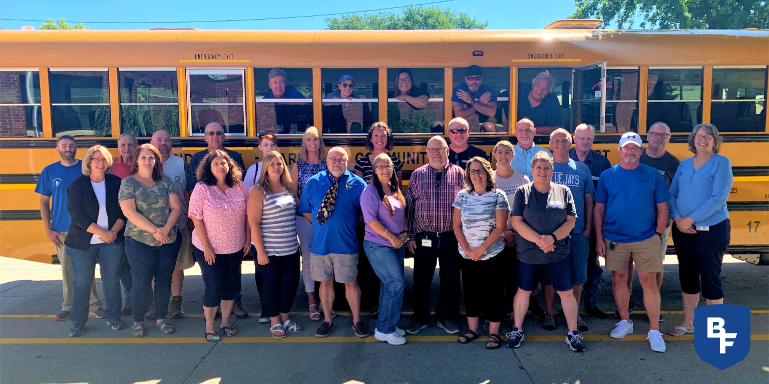 Members of transportation department taking group photo in front of a parked school bus.
